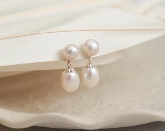 May include: A pair of drop earrings featuring two white pearls each. The top pearl is round and sits directly on the ear, while the bottom pearl is oval-shaped and hangs from a small silver-toned metal cap, creating a delicate dangling effect.