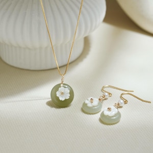 May include: A green jade necklace and earrings set featuring a white flower design. The necklace has a delicate gold chain and the earrings have small pearl accents.