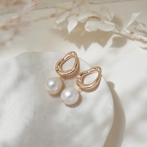 May include: Gold earrings with a unique, irregular shape and a single pearl dangling from each earring.
