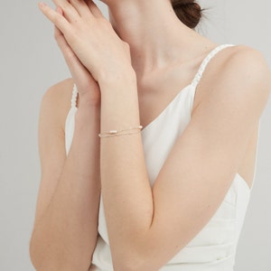 May include: A delicate gold chain bracelet with small white pearls. The bracelet is layered with a second, thinner chain.