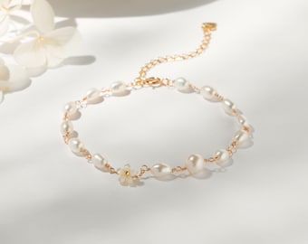 May include: A delicate gold chain bracelet with a small flower charm and white pearl beads.
