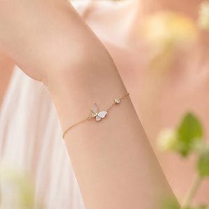 Peut inclure: Un bracelet à chaîne fine en or orné d'un petit pendentif papillon avec une incrustation blanche irisée et une pierre ronde transparente. Le bracelet est composé d'une chaîne à maillons délicats et d'un fermoir, offrant un design raffiné.