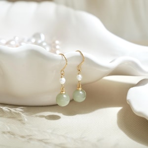 May include: A pair of gold dangle earrings with a green stone and a white pearl on each earring.