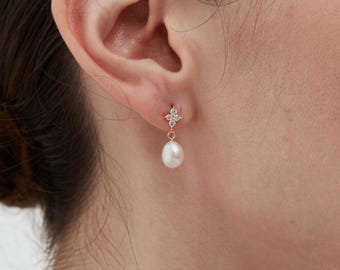 May include: Gold earrings with a small cluster of clear cubic zirconia stones and a single white pearl dangling from the bottom.