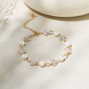 May include: A gold bracelet with a delicate chain and small pearl accents. Each pearl is surrounded by a small, clear crystal leaf design.