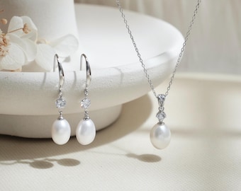 May include: A set of pearl jewellery featuring a silver necklace with a pearl pendant and a pair of silver earrings with pearl drops. Each piece has a small clear crystal accent.