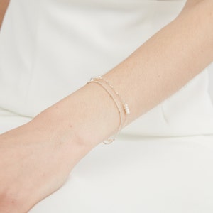 May include: A silver chain bracelet with small white pearls. The bracelet is layered with two chains.