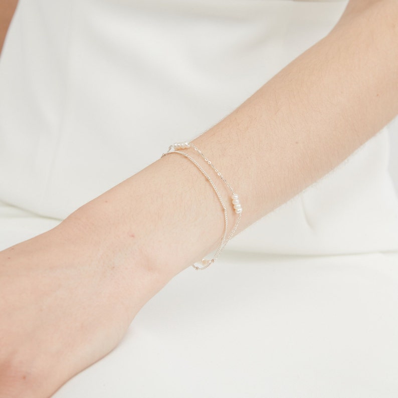 May include: A silver chain bracelet with small white pearls. The bracelet is layered with two chains.