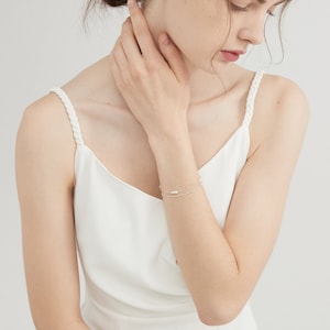 May include: A delicate silver chain bracelet with small pearl accents. The bracelet is layered with a second, thinner chain.