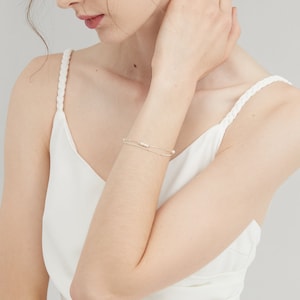 May include: A delicate silver bracelet with a row of small white pearls. The bracelet is layered with a thinner silver chain.