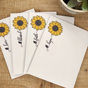 May include: Four white cards with a yellow sunflower and black text. The text on the cards reads "love", "blessed", "faith", and "hope".