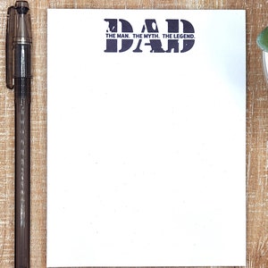 May include: White notepad with a black and white graphic of the word "DAD" with the text "THE MAN. THE MYTH. THE LEGEND." underneath. A black pen is on the left side of the notepad.