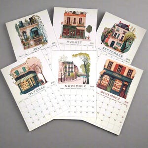 May include: A set of 2025 calendar cards featuring illustrated scenes of Parisian buildings and shops. Each card has a different month and a colorful illustration of a building with a shop front. The illustrations are in a whimsical style with a vintage aesthetic.