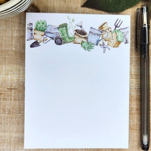 May include: A white notepad with a border of watercolor illustrations of gardening tools and plants. The border includes a watering can, a pair of gardening gloves, a trowel, a rake, a potted plant, and a pair of green rubber boots.