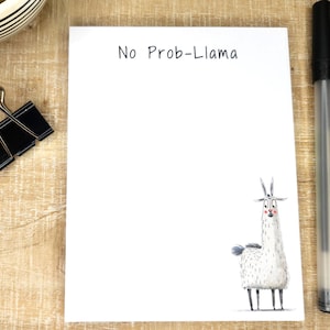 May include: A white notepad with the text "No Prob-Llama" printed on the top. A cartoon llama with a white body and black legs is illustrated at the bottom of the notepad.