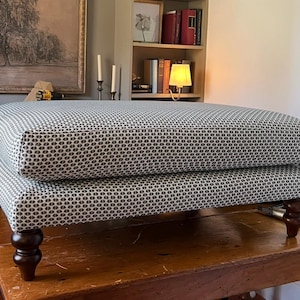 May include: A rectangular ottoman upholstered in a fabric featuring a repeating geometric pattern in dark blue and white. The piece is supported by four dark brown turned wooden legs, each with a rounded, bulbous shape at the base and top.