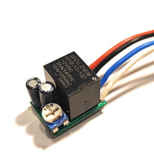 Op de afbeelding: Een groene printplaat met een zwarte relaismodule, twee condensatoren en een blauwe potentiometer. De relaismodule heeft de tekst "GOLDEN GYB-1C-12D 12VDC 20A/14VDC 10A/120VAC C2022-D" erop gedrukt.