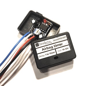 Puede incluir: Una caja negra con una etiqueta blanca que dice "Deselectra deselectra.com Airbag timer Delay: 1 to 10sec Out: 1A 12V". La caja tiene un LED rojo y una pequeña placa de circuito dentro.