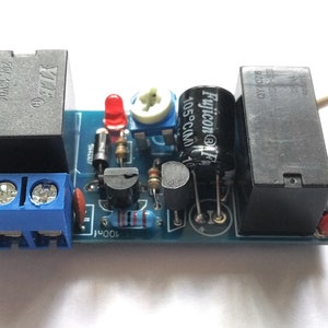 May include: A blue circuit board with two black relays, a red LED, a potentiometer, a capacitor, and a blue terminal block. The board has the text "Fujicon@1F 105°C/10A" printed on it.