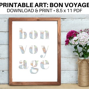 Puede incluir: Arte de pared imprimible con la frase "bon voyage" en letras blancas sobre un fondo de mapa del mundo. El arte está enmarcado en un marco de madera marrón y se muestra en una pared de madera blanca.