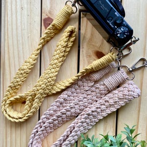 May include: Two camera straps made of braided rope. One strap is yellow and the other is a light pink color. Both straps have metal clasps.