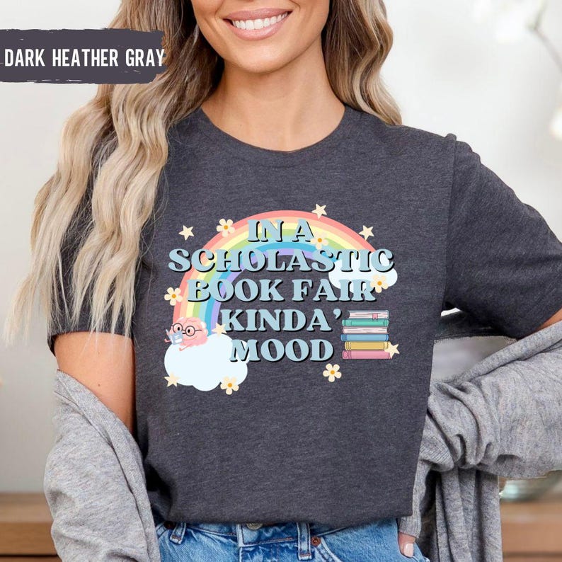 Puede incluir: Camiseta gris oscuro jaspeada con un arco&iacute;ris, estrellas y el texto "In a Scholastic Book Fair Kinda' Mood".