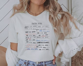 May include: White t-shirt with a black and white graphic of a vintage due date chart. The chart lists dates from September 1970 to June 1972.