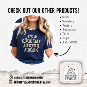 Pu&ograve; includere: Una maglietta blu navy con il testo "It's a good day to read a book" in lettere colorate con accenti floreali. La maglietta &egrave; indossata da una persona. L'immagine include anche un logo per il negozio, "Bright-Eyed & Bookish", con un libro e fiori.