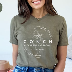 May include: A green t-shirt with a white graphic of a seashell and the text "The Conch Leadership Academy Est. 1954 Leader-Hunter-Survivor" in a circle.