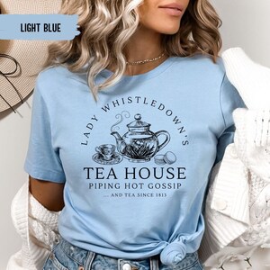 May include: Light blue t-shirt with a black and white illustration of a teapot, teacup, and macarons. The text reads "Lady Whistledown's Tea House Piping Hot Gossip...and Tea Since 1813"