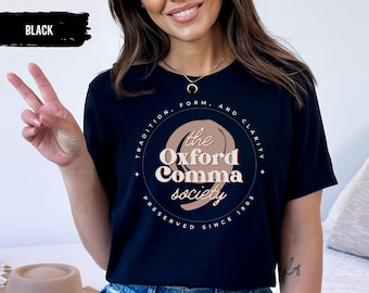 May include: Black t-shirt with a brown and white graphic design that says "The Oxford Comma Society" with the text "Tradition, Form, and Clarity Preserved Since 1905" around the graphic.