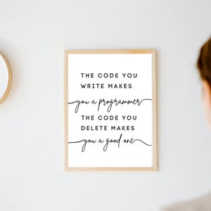 May include: A framed print with the text "THE CODE YOU WRITE MAKES you a programmer THE CODE YOU DELETE MAKES you a good one" in black script. The frame is a light wood color, and a clock is visible in the background.