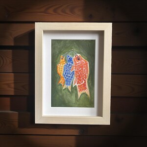 May include: A framed watercolor painting of three colorful carp kites, in orange, blue, and red, hanging against a green background. The artwork is displayed in a light wood frame, perfect for home decor.