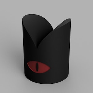 May include: A black cylindrical container with a cat-eye design. The container has a red eye graphic on the side. The top of the container has a curved, pointed shape.