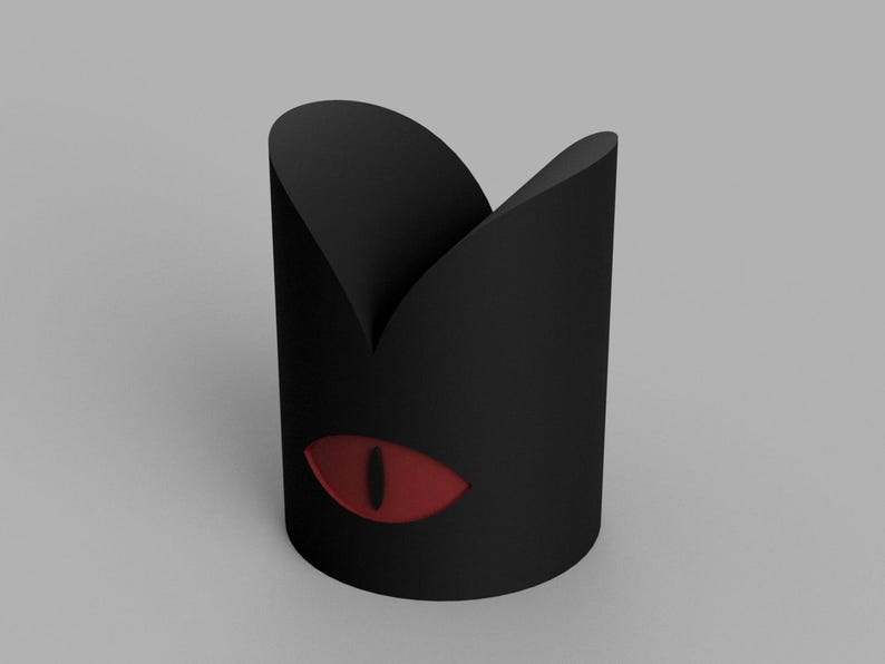 May include: A black cylindrical container with a cat-eye design. The container has a red eye graphic on the side. The top of the container has a curved, pointed shape.