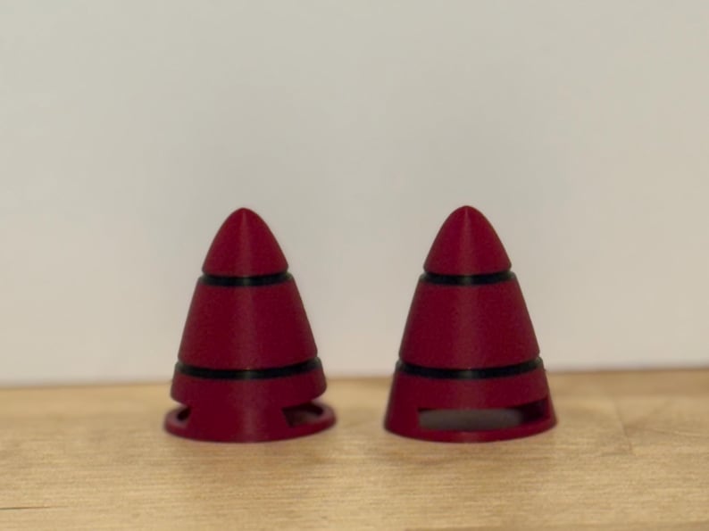 May include: Two maroon-colored, cone-shaped objects with black bands. The objects have a rounded top and a base with cut-out sections. They are placed on a light brown wooden surface.
