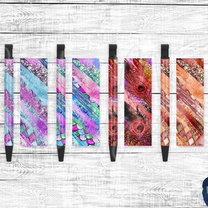 Könnte beinhalten: Fünf schwarze Stifte mit verschiedenen bunten Designs. Die Designs beinhalten Glitzer, abstrakte Muster und eine Pfauenfeder.