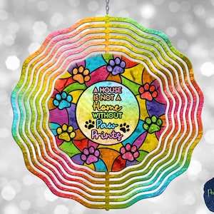 Puede incluir: Un molinillo de viento decorativo con borde arcoíris y diseño central. El diseño presenta huellas de patas y el texto "A HOUSE IS NOT A HOME WITHOUT Paw Prints". El fondo tiene un efecto de vidriera.