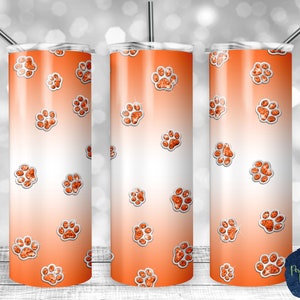 Op de afbeelding: Een roestvrijstalen beker met een oranje en witte gradiënt achtergrond. De beker is versierd met meerdere oranje glitter pootafdrukken. Een zilveren rietje is in het deksel gestoken. Een geweldig cadeau voor dierenliefhebbers.