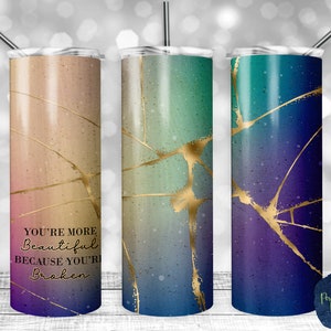 May include: Three stainless steel tumblers with a gradient color design and gold crackle effect. The tumbler on the left has the text "You're more beautiful because you're broken".