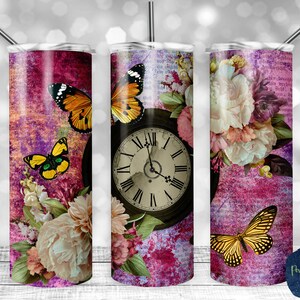 May include: Three stainless steel tumblers with a pink and purple floral design. Each tumbler features a different butterfly and a vintage clock face. The tumblers are perfect for adding a touch of whimsy to your everyday routine.