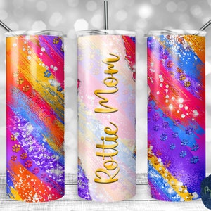 May include: Three stainless steel tumblers with colorful abstract designs and glitter accents. The center tumbler has the name "Rottie Mom" in gold lettering.