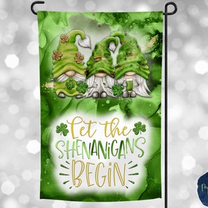 May include: A green garden flag with three gnomes wearing green hats and holding shamrocks. The flag has the text "Let the Shenanigans Begin" in gold lettering.