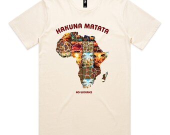May include: Cream-colored t-shirt featuring the words "HAKUNA MATATA" in red above a colorful map of Africa. The phrase "NO WORRIES" is printed below the map. The shirt has a crew neck and short sleeves.
