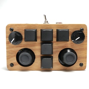 May include: A rectangular wooden control device featuring a light brown wood grain finish. It includes five black square mechanical keys, two black rotary knobs with white indicators, two black circular joysticks, and a metal toggle switch.