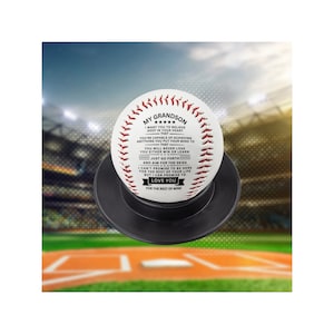 May include: White baseball with black stitching and red seams. The ball has a message printed on it that reads "My Grandson" and includes a heartfelt message about believing in yourself and aiming for the skies. The ball is sitting on a black stand.