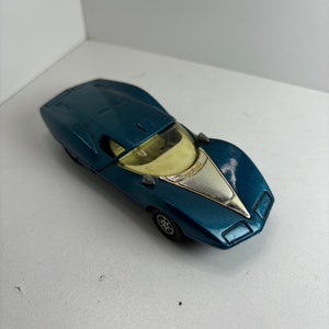 May include: A vintage blue toy car with a silver front detail and a yellow windshield. The toy car has a sleek, aerodynamic design and small black wheels. The car is a classic collectible item.