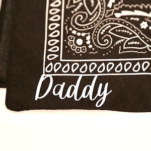 May include: Black bandana with a white paisley pattern and the word "Daddy" written in white cursive.