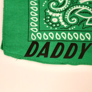 May include: Green bandana with a white paisley pattern and the word "DADDY" printed in black.