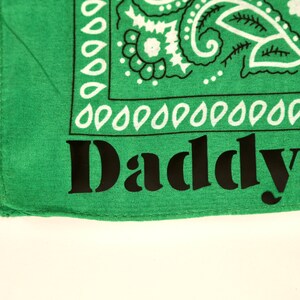 May include: Green bandana with a white paisley pattern and the word "Daddy" printed in black.